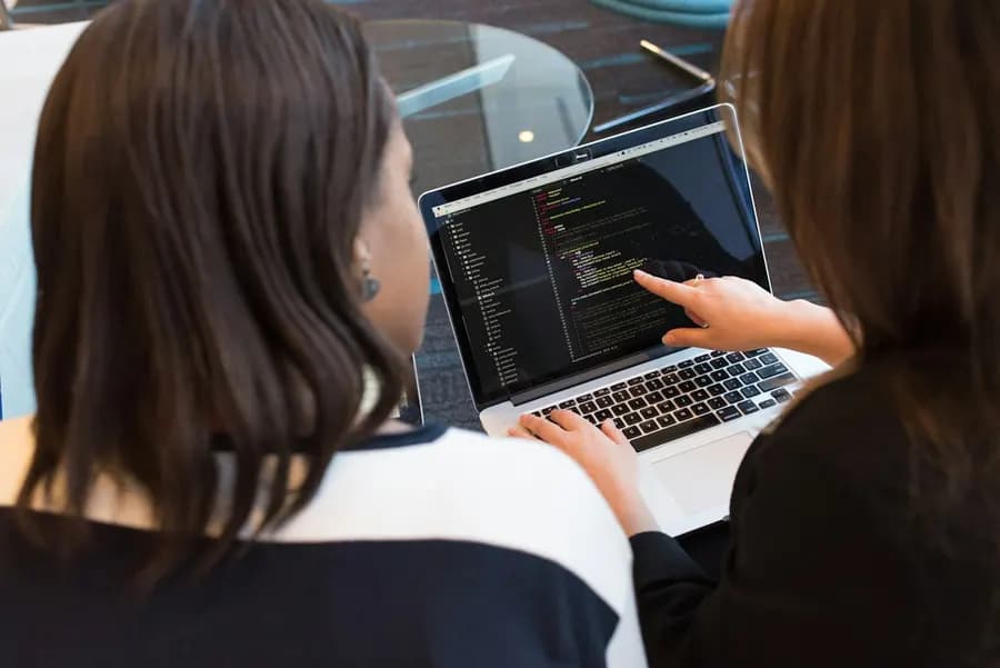 A woman reviewing code on a laptop with a colleague