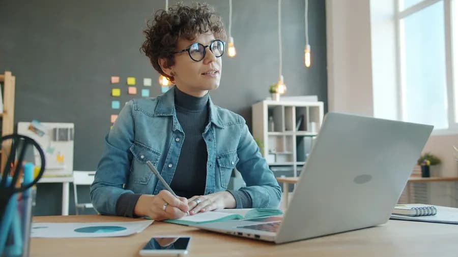 A woman planning work at her desk with a laptop and notebook